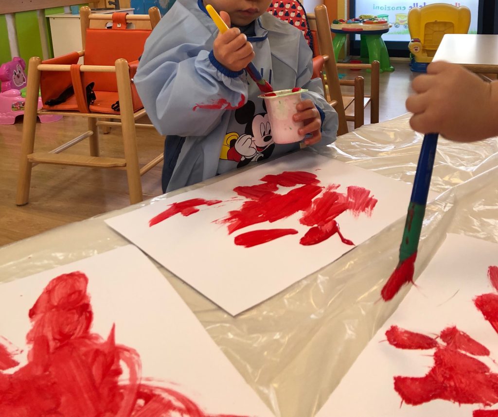 Bambino che dipinge con pittura rossa.